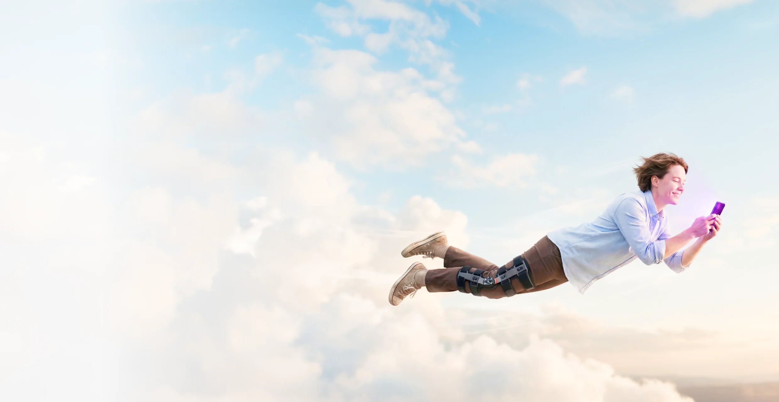 A smiling patient in a knee brace flying through the clouds while looking at their phone